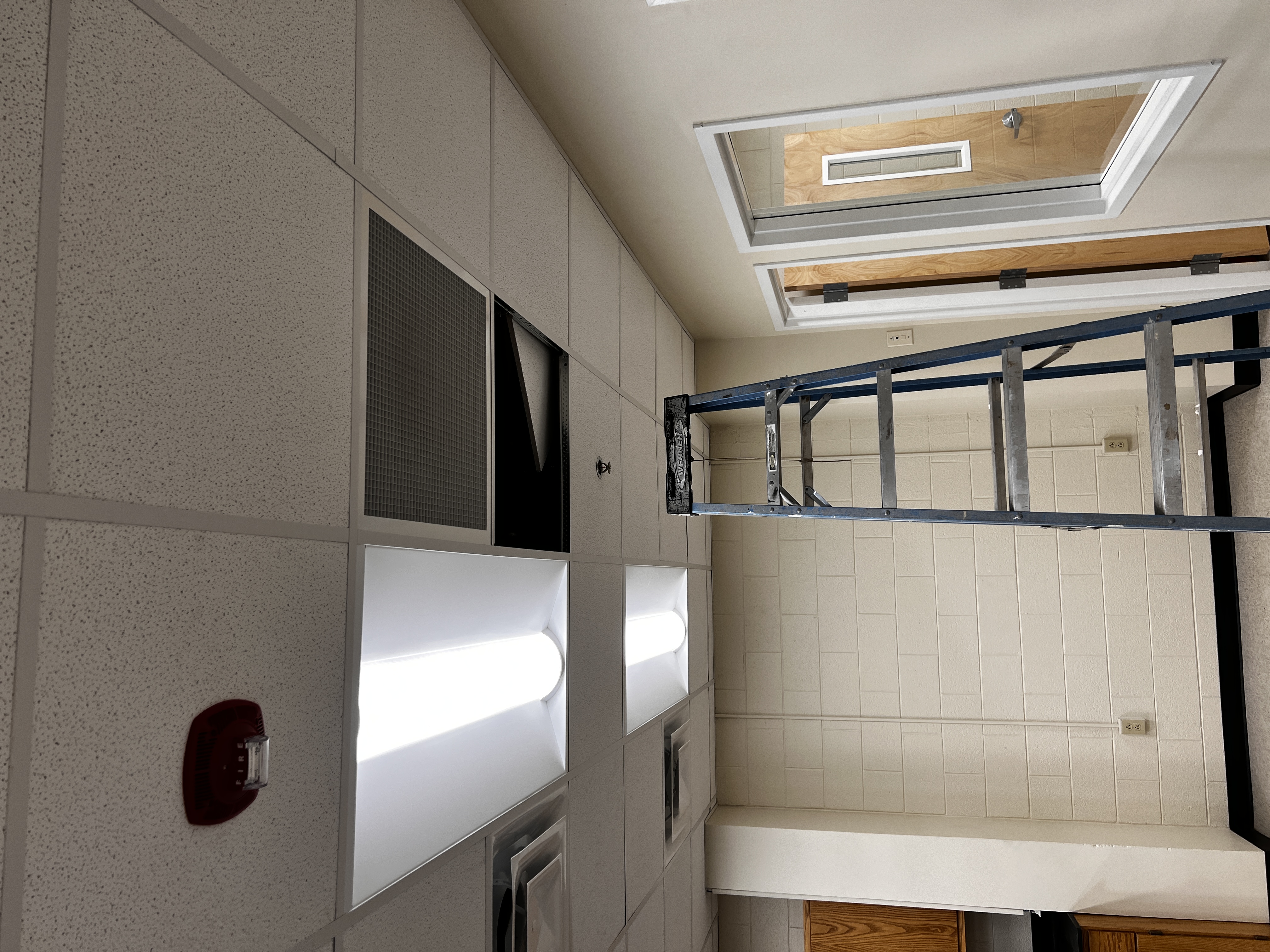 Hallway in a lab building, with one ceiling tile shifted over and a ladder leading up to it.